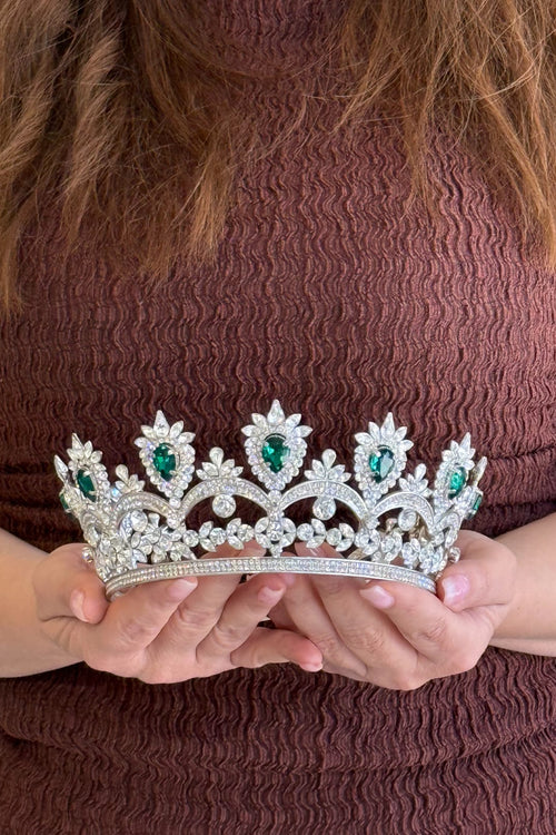 model holding a decorative tiara with green gemstones against a brown background