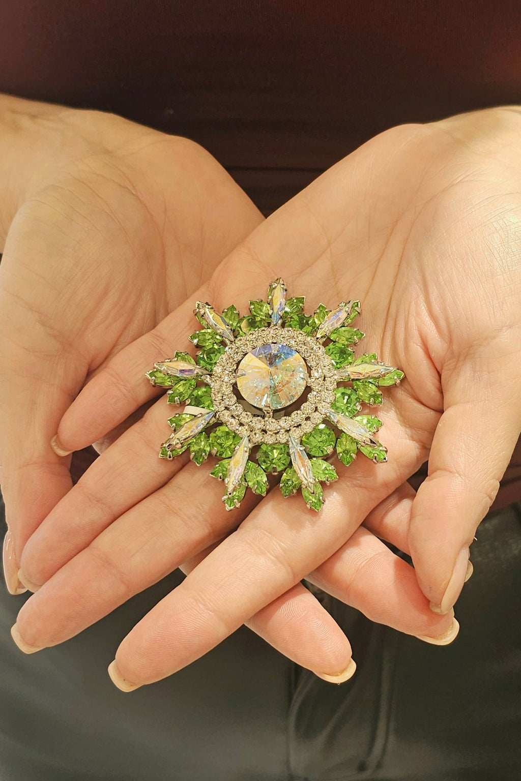 Hand holding a decorative brooch with green gemstones and gold accents.
