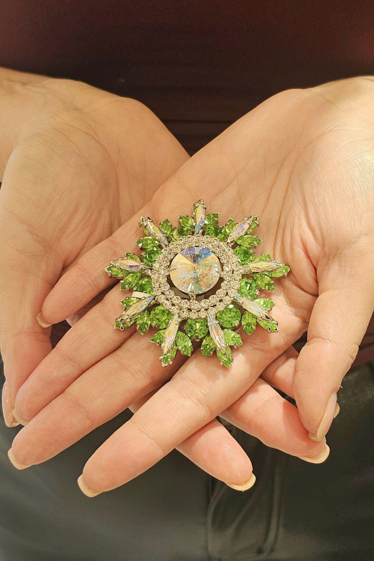 Hand holding a decorative brooch with green gemstones and gold accents.