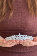 Close-up of a model holding a magnificent, handcrafted silver tiara featuring a prominent central crystal sunburst blossom flanked by dense, symmetric rows of marquise crystals.