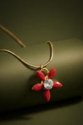 Red stellar flower pendant necklace with a gold chain and a central clear crystal, displayed against an olive green background.