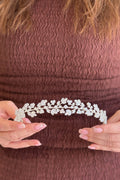 Close-up of a model holding a delicate, low-profile silver bridal headpiece featuring symmetrical branches of shimmering marquise crystal leaves meeting gracefully in the center.