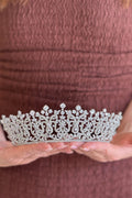 Close-up of a model holding a luxury handcrafted gold tiara shaped into detailed laurel leaf clusters encrusted with shimmering olivine and olive-green crystals.