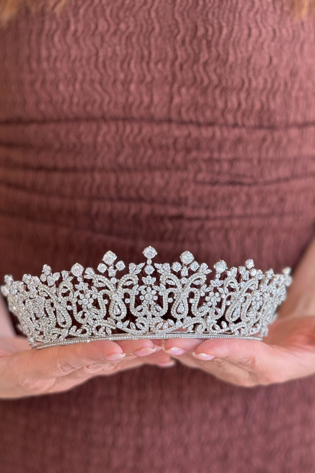 Close-up of a model holding a luxury handcrafted gold tiara shaped into detailed laurel leaf clusters encrusted with shimmering olivine and olive-green crystals.