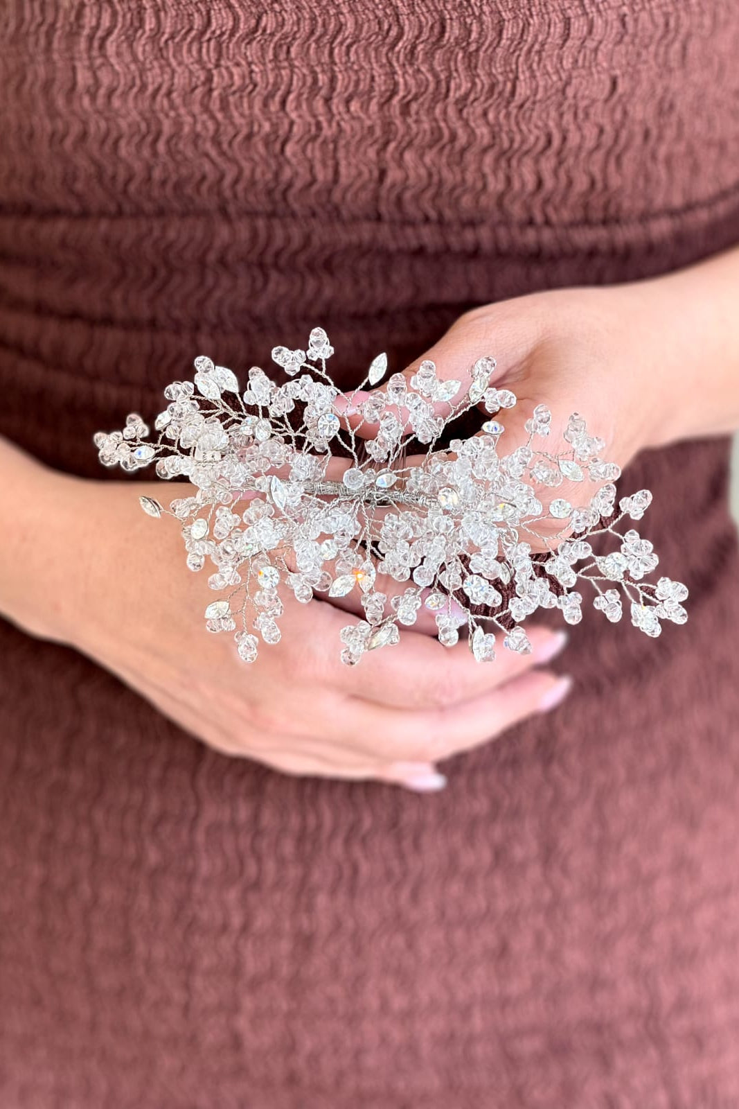 Close-up of a model holding a handcrafted silver wire bridal hair vine intricately woven with delicate clusters of tiny clear crystals resembling blooming baby's breath.