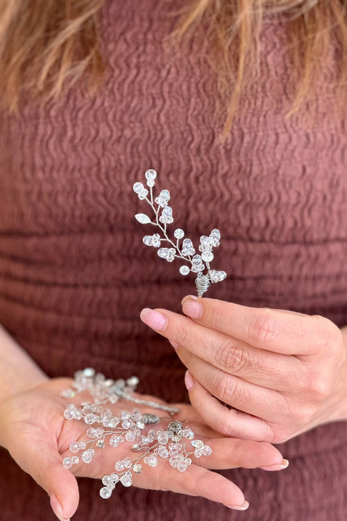 Close-up of a model holding a delicate, handcrafted silver wire hair sprig featuring organic branching stems set with clear faceted crystal beads and dainty marquise leaves.