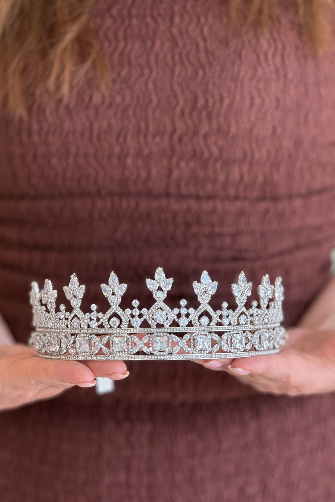 Close-up of a model holding a stately, handcrafted silver bridal tiara featuring a structured base of square-cut panels topped with an open-work lattice of crystal arches and sharp fleur-de-lis peaks.