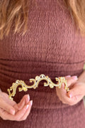 Close-up of a model holding a soft, handcrafted gold-plated headpiece featuring open arabesque scrolls lined with pavé crystals and accented with delicate champagne teardrop stones