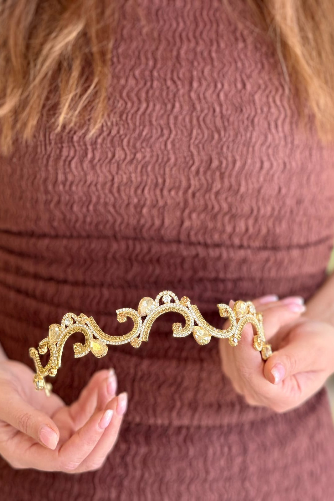 Close-up of a model holding a soft, handcrafted gold-plated headpiece featuring open arabesque scrolls lined with pavé crystals and accented with delicate champagne teardrop stones