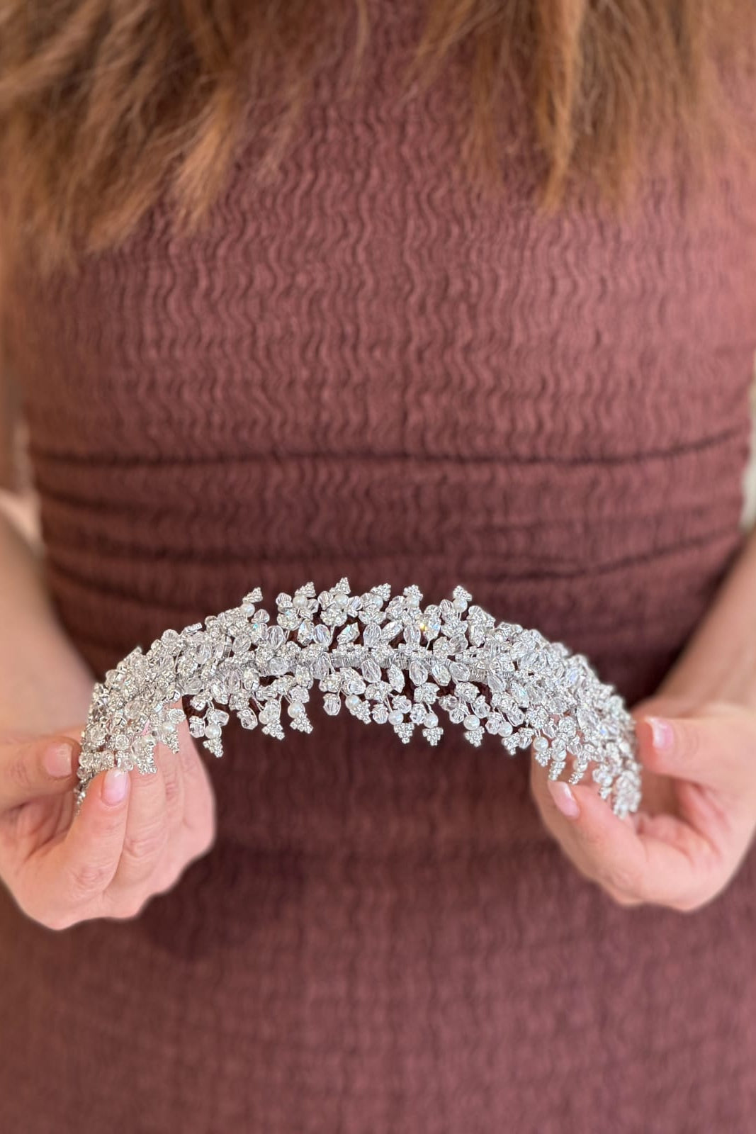 Close-up of a model holding a wide-profile, handcrafted bridal tiara intricately paved with dense crystal lace patterns, swirling arabesque arches, and prominent pointed peaks.