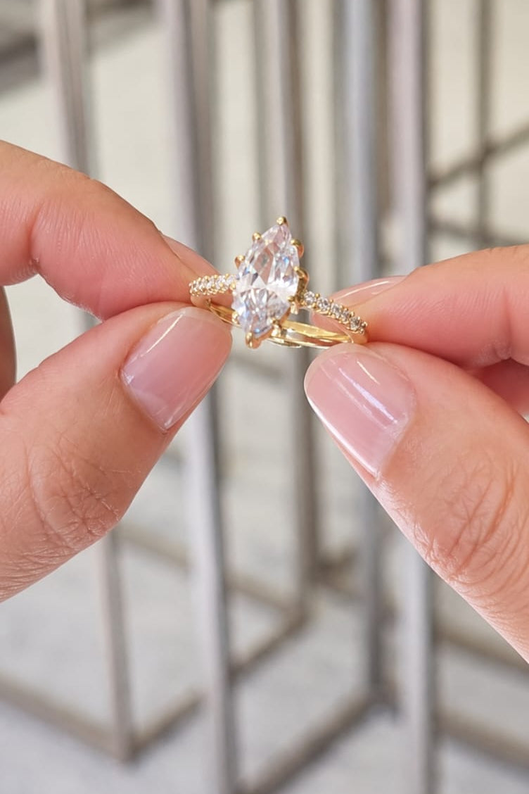 Hand holding a gold ring with a large diamond against a blurred background