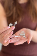 Close-up of a model holding delicate silver bridal hairpins featuring dainty floral and leaf motifs hand-set with clear marquise crystals.