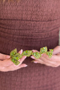 Close-up view of a model holding a handcrafted gold-plated tiara featuring an intricate leaf vine pattern densely encrusted with shimmering peridot and olive green crystals.