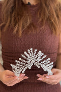 Close-up of a model holding a towering handcrafted silver bridal tiara structured with geometric crystal branches radiating outward like traditional palm fronds