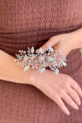 Close-up of a model holding a handcrafted silver wire bridal hair piece intricately woven with blush pink crystal flowers, pavé-set leaves, and shimmering pastel bead sprays.