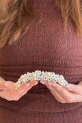 Close-up of a model holding a thick, handcrafted bridal headpiece densely packed with a dimensional cluster of white pearls and clear crystal beads.