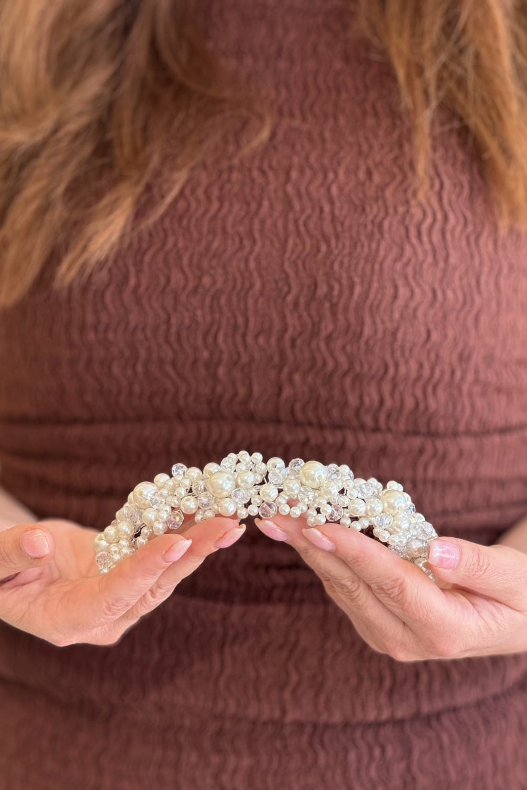 Close-up of a model holding a thick, handcrafted bridal headpiece densely packed with a dimensional cluster of white pearls and clear crystal beads.