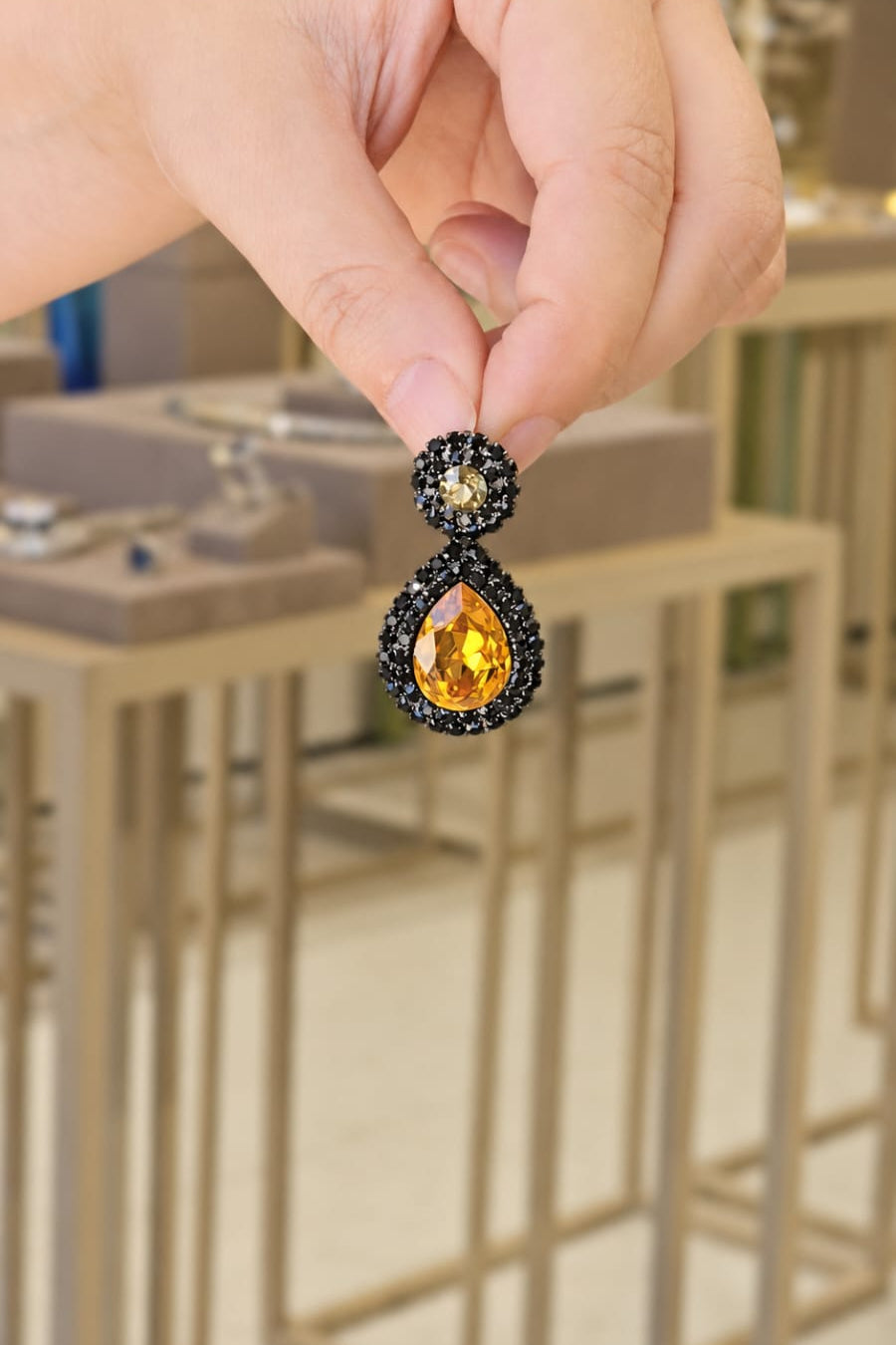 Earring with a gold gemstone held by a hand against a blurred background