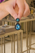 Hand holding a pair of earrings with blue gemstones in a store setting