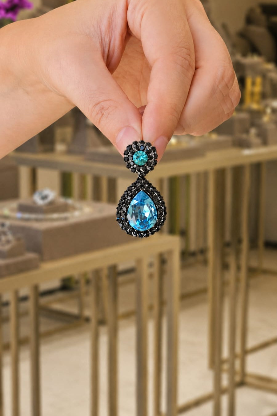 Hand holding a pair of earrings with blue gemstones in a store setting