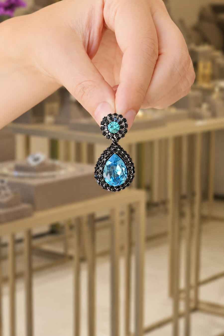 Teardrop-shaped earrings with 
 turquoise gemstones held by a hand in an indoor setting.