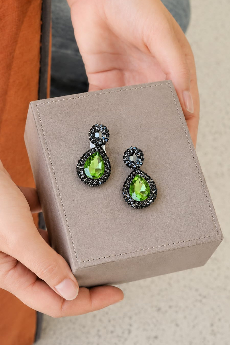 Green gemstone earrings in a jewelry box held by hands.