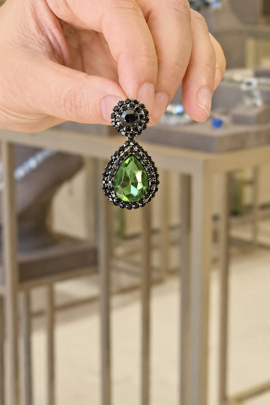 Green teardrop earring held by a hand with a blurred background