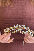 Close-up of a model holding a delicate, handcrafted gold wire bridal tiara sculpted like winding vines with starburst clusters of marquise and baguette crystals 
