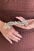 Close-up of a model holding a handcrafted gold-plated tiara beautifully arranged with brilliant, clear marquise and round crystals in a sweeping floral vine pattern.