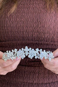 Close-up of a model holding a spectacular, handcrafted silver bridal tiara featuring complex, open-work geometric floral and snowflake clusters fully set with shimmering round crystals