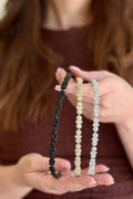 Three beaded headbands in black, gold, and silver held by a person with blurred background