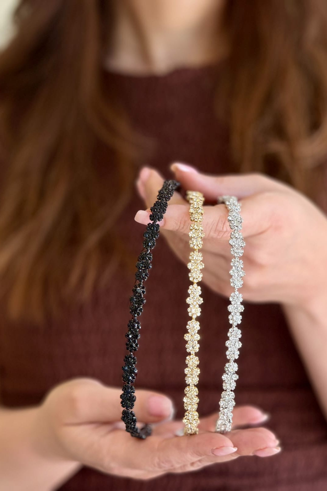 Three beaded headbands in black, gold, and silver held by a person with blurred background